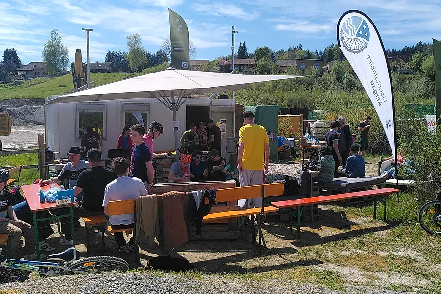 Festbetrieb am Eröffnungstag: Besucher an Bierbänken vor dem Container, Grillstelle, Kinder mit Bikes.