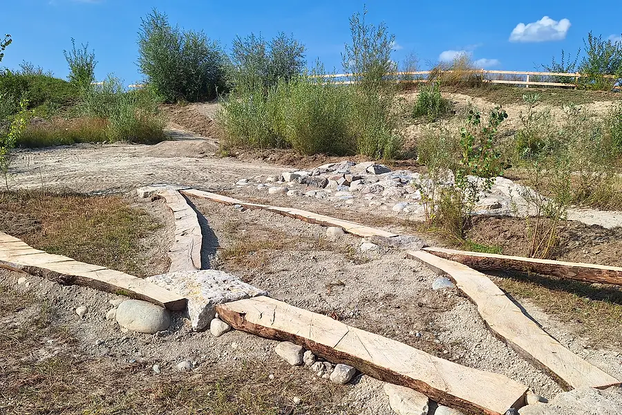 Erste Holzbalken und ein mit Flusssteinen gefasstes Element auf dem bereits modellierten Gelände.